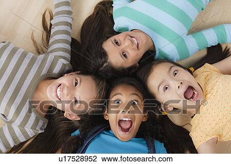 Stock Image - Studio portrait of four girls (8-9) lying on floor. Fotosearch
