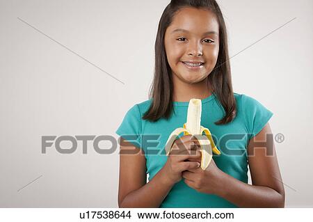 Picture - Studio portrait of girl (10-11) holding banana. Fotosearch