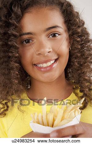 Picture - Studio portrait of girl (10-11) holding french fries. Fotosearch