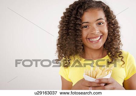 Stock Photo - Studio portrait of girl (10-11) holding french fries. Fotosearch