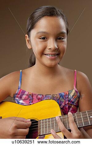 Stock Image - Studio portrait of girl (10-11) playing guitar. Fotosearch