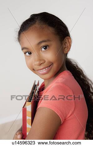 Stock Image - Studio portrait of girl (8-9) holding books. Fotosearch