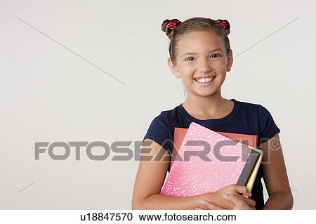 Stock Image - Studio portrait of girl (8-9) holding books. Fotosearch