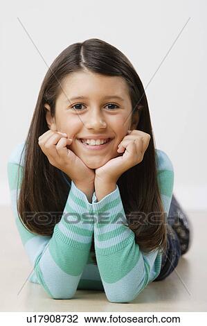 Stock Image - Studio portrait of girl (8-9) lying on floor. Fotosearch