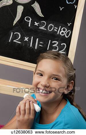 Stock Image - Studio portrait of girl (8-9) next to blackboard. Fotosearch