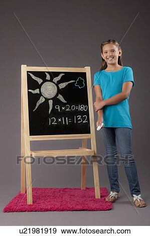 Stock Photo - Studio portrait of girl (8-9) standing next to blackboard. Fotosearch