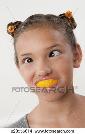 Picture - Studio portrait of girl (8-9) with slice of lemon in mouth. Fotosearch