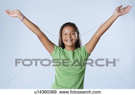 Stock Photo - Studio portrait of girl smiling (10-11) with raised hands. Fotosearch