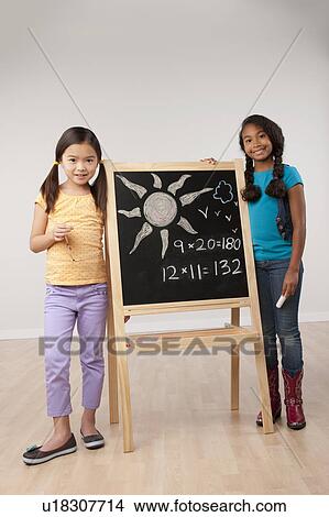 Studio portrait of two girls (8-9) standing by blackboard View Large Photo Image Picture - Studio portrait of two girls (8-9) standing by blackboard. Fotosearch