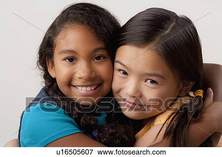 Stock Photo - Studio portrait of two girls (8-9) embracing. Fotosearch
