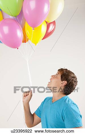 Stock Image - Studio shot of boy (12-13) holding bunch of balloons. Fotosearch