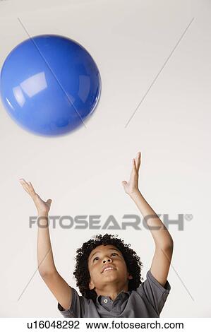 Stock Image - Studio shot of boy (8-9) tossing blue ball. Fotosearch