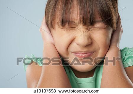 Stock Photo - Studio shot of girl (10-11) with closed eyes covering ears. Fotosearch