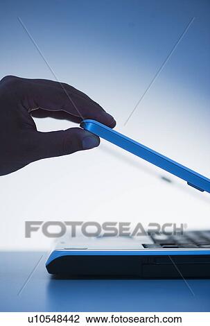 Stock Image - Studio shot of hand opening laptop. Fotosearch