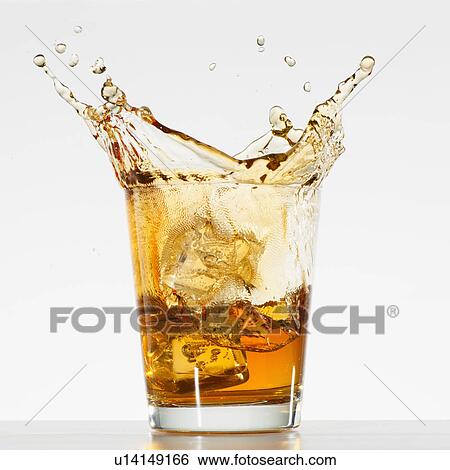 Stock Photograph - Studio shot of ice cubes splashing into glass of whiskey. Fotosearch