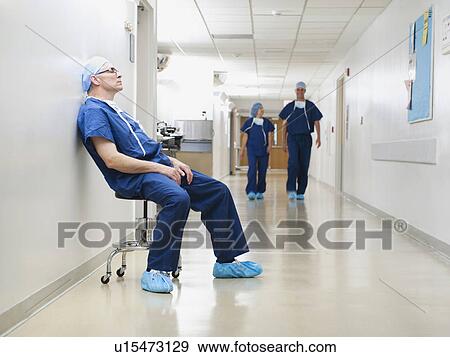 Stock Photo - Surgeon resting in hospital corridor after operation, while two of his colleagues are walking in background. Fotosearch