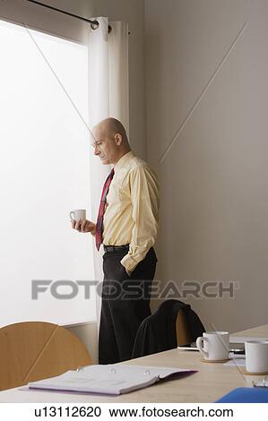 Thoughtful businessman standing in board room and holding mug View Large Photo Image Stock Image - Thoughtful businessman standing in board room and holding mug. Fotosearch