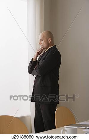 Thoughtful businessman standing in board room View Large Photo Image Stock Image - Thoughtful businessman standing in board room. Fotosearch