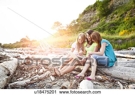 Stock Image - Three young women hanging out on beach. Fotosearch