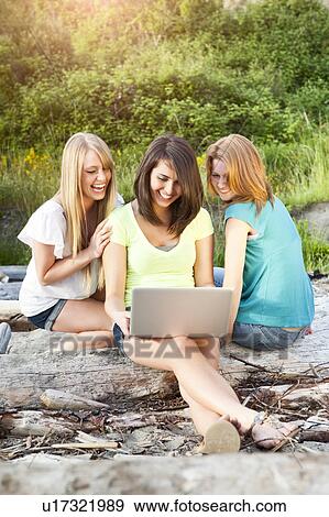 Stock Photo - Three young women hanging out on beach, using laptop. Fotosearch