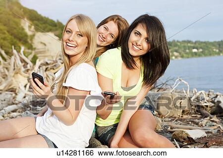 Three young women hanging out on beach, using cell phones View Large Photo Image Stock Photograph - Three young women hanging out on beach, using cell phones. Fotosearch