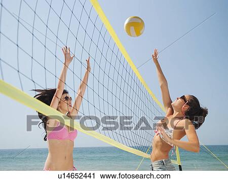Stock Image - Two attractive young women playing beach volleyball . Fotosearch
