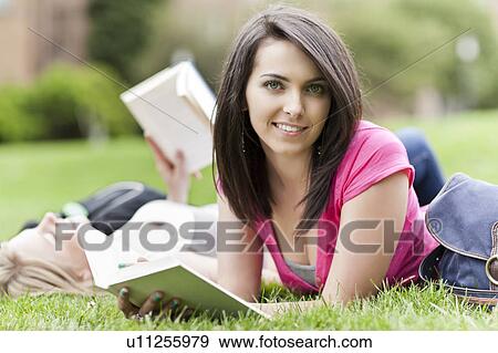 Stock Photo - Two female college student lying on grass reading books, one looking at camera. Fotosearch