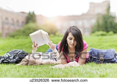 Stock Photograph - Two female college student lying on grass reading books. Fotosearch