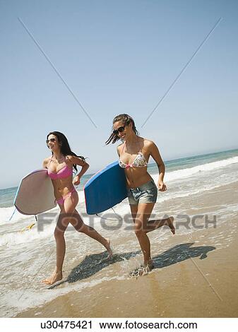 Two young attractive women running into water with swimming boards View Large Photo Image Stock Image - Two young attractive women running into water with swimming boards. Fotosearch