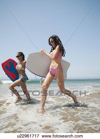 Two young attractive women running into water with swimming boards View Large Photo Image Stock Photo - Two young attractive women running into water with swimming boards. Fotosearch