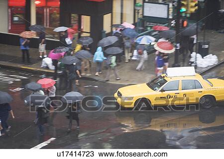 Stock Image - USA, New York State, New York City, Manhattan, Yellow taxi cab on street, pedestrians walking with umbrellas. Fotosearch