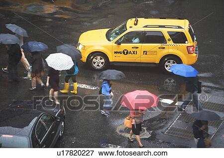 Stock Photo - USA, New York State, New York City, Manhattan, Yellow taxi cab on street, pedestrians walking with umbrellas. Fotosearch