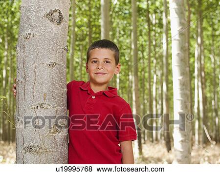Stock Photo - USA, Oregon, Boardman, Boy (8-9) standing between poplar trees in tree farm. Fotosearch