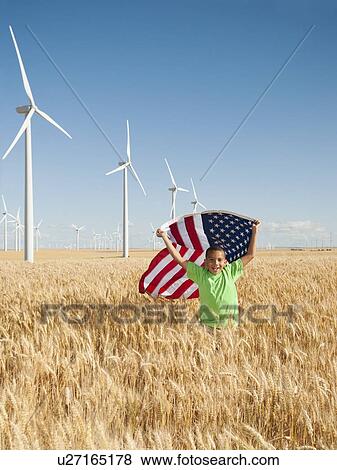 Stock Photo - USA, Oregon, Wasco, Boy (8-9) flying american flag in wheat field with wind turbines in background. Fotosearch
