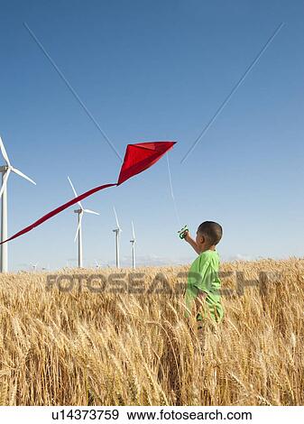 Stock Photo - USA, Oregon, Wasco, Boy (8-9) playing with kite in wheat field, wind turbines in background. Fotosearch