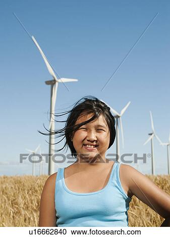 Stock Image - USA, Oregon, Wasco, Cheerful girl (10-11) standing in wheat field with wind turbines in background. Fotosearch