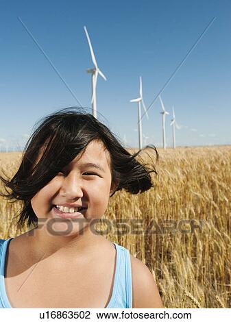 Stock Image - USA, Oregon, Wasco, Cheerful girl (10-11) standing in wheat field with wind turbines in background. Fotosearch