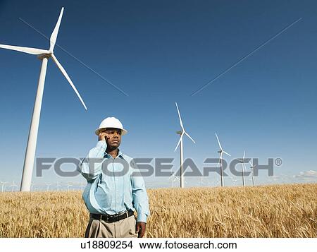 USA, Oregon, Wasco, Engineer standing in wheat field in front of wind turbines, using mobile phone View Large Photo Image Picture - USA, Oregon, Wasco, Engineer standing in wheat field in front of wind turbines, using mobile phone. Fotosearch