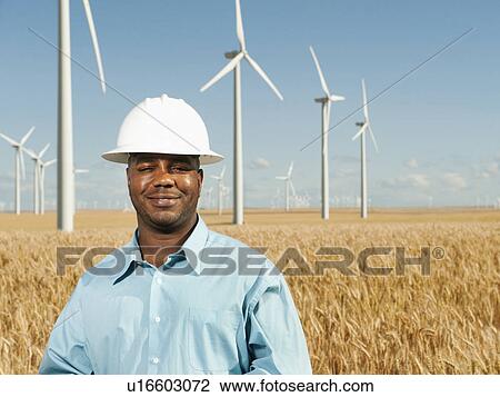 Stock Image - USA, Oregon, Wasco, Engineer standing in wheat field in front of wind turbines. Fotosearch