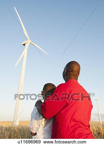 Stock Photo - USA, Oregon, Wasco, Father and son (8-9) standing in wheat field, watching wind turbine. Fotosearch
