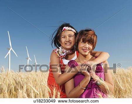 Stock Photo - USA, Oregon, Wasco, Girl (10-11) and mother standing in wheat field in front of wind turbines. Fotosearch