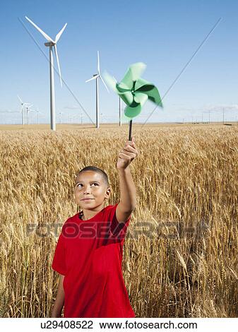 Stock Image - USA, Oregon, Wasco, Girl (10-11) holding fan in wheat field with wind turbines in background. Fotosearch