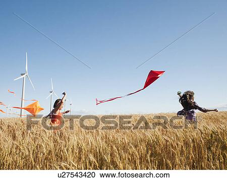 Stock Image - USA, Oregon, Wasco, Girls (10-11, 12-13) playing with kite in wheat field, wind turbines in background. Fotosearch