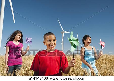 Stock Photograph - USA, Oregon, Wasco, Pre-teen girls (10-11) and boy (8-9) holding fans in wheat field in front of wind turbines. Fotosearch
