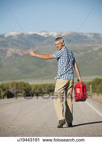 Stock Image - USA, Utah, Kanosh, Mid adult man carrying empty canister attempting to stop vehicles for help. Fotosearch