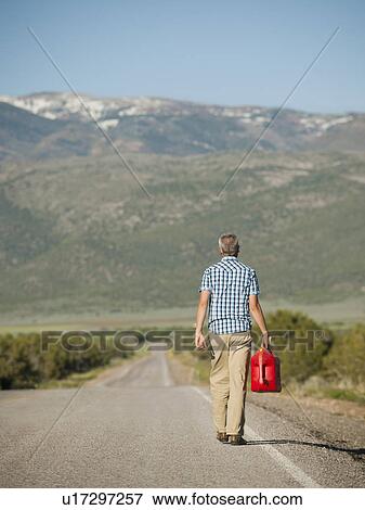 Stock Photo - USA, Utah, Kanosh, Mid adult man carrying empty canister along empty road. Fotosearch