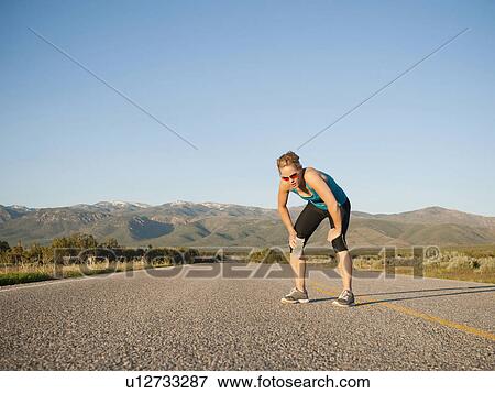 Stock Photo - USA, Utah, Kanosh, Mid adult woman taking break from running on empty road. Fotosearch