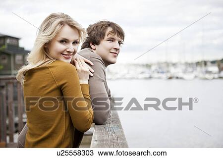 Stock Image - USA, Washington, Seattle, Young couple on pier, woman looking at camera. Fotosearch