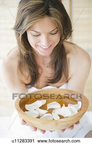 Stock Image - Woman in spa holding bowl with flower petals. Fotosearch