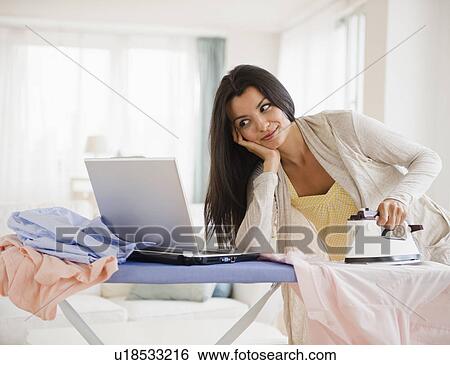 Stock Photograph - Woman ironing and using laptop. Fotosearch